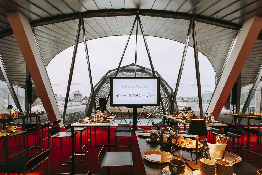 Gedeckte Tische in einer modernen Location mit Blick auf den Berliner Reichstag für ein Politisches Frühstück der Organisationen gfi Europe, ProVeg International und BALPro.